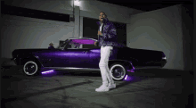 a man standing next to a purple car with purple lights