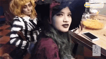 two women dressed in halloween costumes are sitting at a table with a sign that says uk 48 on it