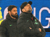 a man wearing a jacket that says ' axa ' on it stands next to another man