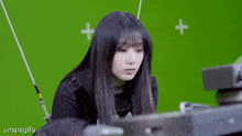 a woman is standing in front of a green screen while holding a piece of equipment .