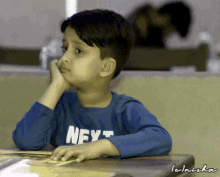 a little boy wearing a blue shirt that says next