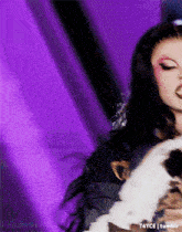 a woman is holding a cat in front of a purple background