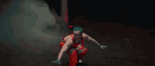 a man with blue hair is dancing in a dark room with red smoke coming out of a building .