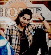 a man in a plaid shirt sits in front of a sign that says happy home
