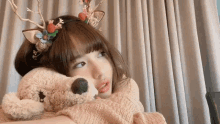 a girl wearing a reindeer headband is holding a stuffed animal