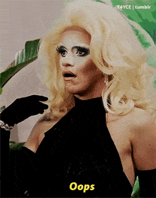 a drag queen with blonde hair and black gloves says the word oops