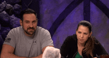 a man and a woman are sitting at a table and the man is wearing an under armour shirt