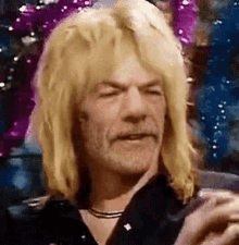 a man with long blonde hair and a beard is holding a glass of beer .