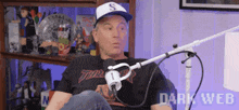 a man wearing a baseball cap is sitting in front of a microphone in a room .