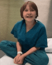 a young girl wearing scrubs is sitting on a bed with her legs crossed and smiling .