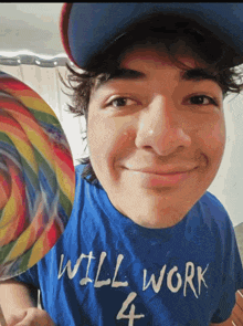a young man wearing a blue shirt that says will work 4 holds a lollipop