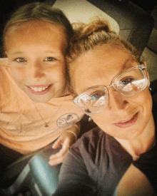 a woman wearing glasses is smiling next to a little girl wearing an orange shirt