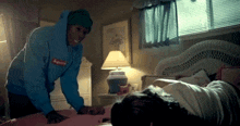 a person wearing a blue supreme hoodie is putting a pillow on a bed