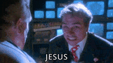 a man in a suit and tie is talking to another man and the word jesus is on the screen