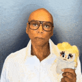 a bald man wearing glasses is holding a stuffed animal with blonde hair