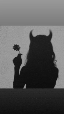 a silhouette of a woman with horns holding a flower .