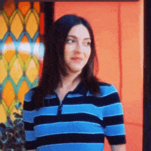 a woman in a blue and black striped shirt is standing in front of an orange wall