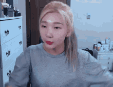 a woman with blonde hair is wearing a grey sweater