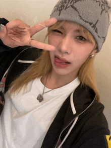 a woman wearing a beanie and a white shirt shows a peace sign