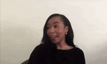 a woman in a black shirt and earrings is sitting in a chair and smiling .