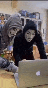 a couple of people wearing masks are looking at a laptop computer .