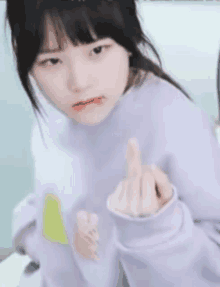 a young girl in a purple sweater is making a middle finger gesture .