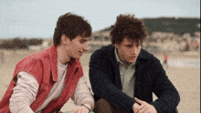two men are sitting on the beach and one has a watch on his wrist