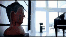 a statue of a buddha sits in a room with a piano