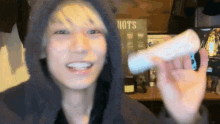 a man in a hooded jacket is holding a white object in front of a sign that says hots
