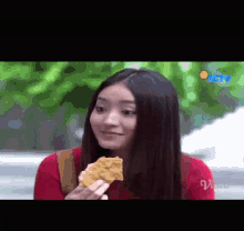 a woman in a red sweater is eating a piece of food .