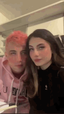 a man and a woman are posing for a picture in a kitchen . the woman has pink hair and the man has red hair .