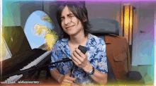 a man in a hawaiian shirt is sitting in front of a piano and holding a cell phone .