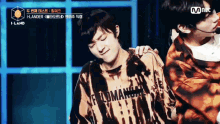 two young men are standing next to each other on a stage . one of the men is wearing a tie dye shirt .