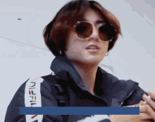 a person wearing sunglasses and a jacket that says fila on the side
