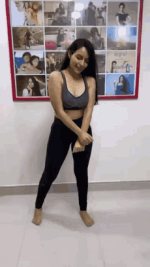 a woman in a sports bra and leggings is dancing in front of a collage of pictures on the wall .