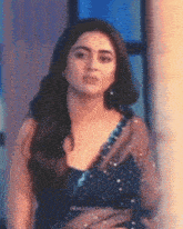 a woman in a saree is standing in front of a window and looking at the camera .