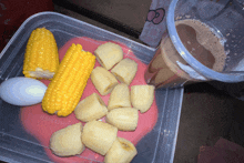 a plastic container with corn on the cob bananas and a cup of milk