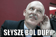 a bald man with a mustache holds his hand to his ear and says seysze bol dupy