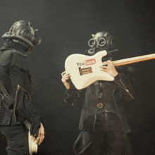 a man in a gas mask is holding a white guitar that says you suck