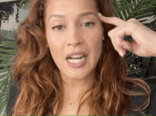 a woman with red hair is holding her finger to her forehead and making a funny face .