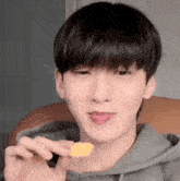 a young man is holding a small piece of food in his hand and eating it .