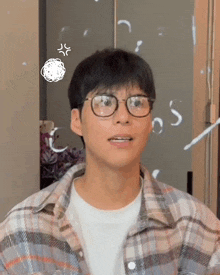 a young man wearing glasses and a plaid shirt is looking at the camera .