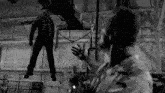 a black and white photo of a man standing next to a chained man hanging from the ceiling .