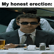 a man in a suit and tie sits at a table with a fork in his hand and the words my honest erection