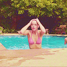 a woman in a pink bikini is standing in the edge of a swimming pool