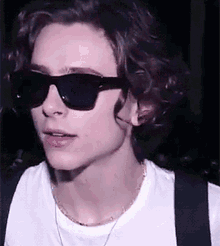 a young man with curly hair wearing sunglasses and a white shirt .