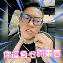 a man wearing glasses and ear buds is giving a thumbs up with chinese writing behind him
