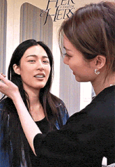 a woman is applying makeup to another woman 's face in front of a sign that says her and hers