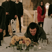 a man sits at a table with flowers and glasses