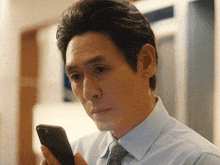 a man in a blue shirt and tie looks at his cell phone
